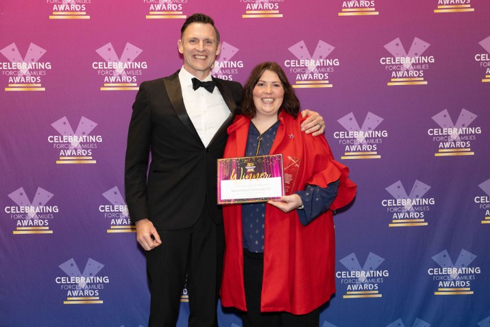 The Founder and CEO of NDC stands smiling with a representative from Pinnacle Service Families at the Celebrating Forces Families Awards. The NDC CEO is holding a winner’s certificate and trophy in front of a branded awards backdrop.