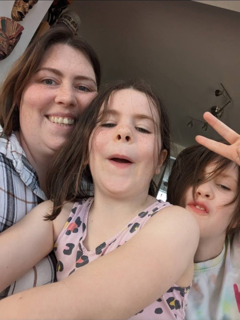 A playful close-up selfie of a woman and two young children indoors.