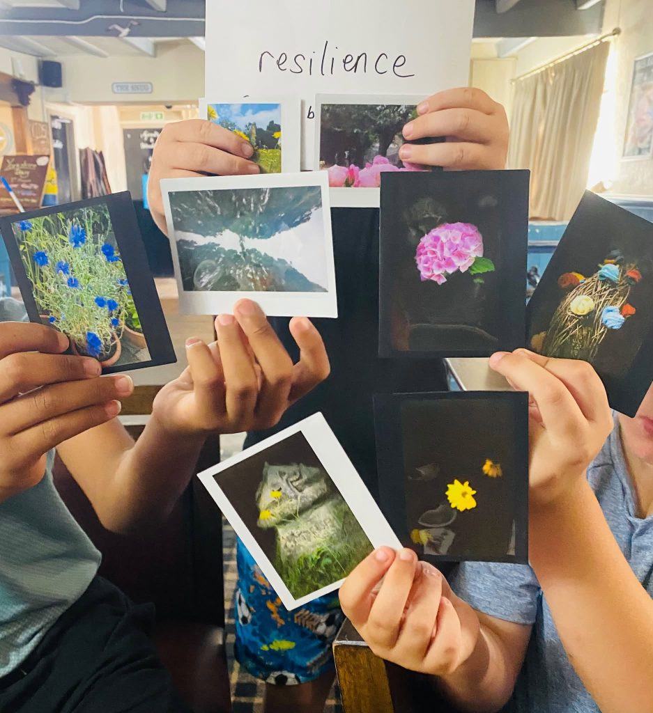 A group of people holding up a collection of instant photo prints centered around a paper sign that reads "resilience".