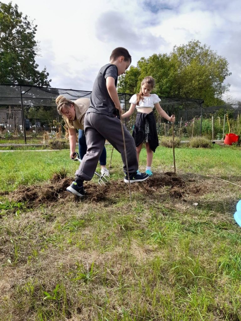 Two children and an adult working together in an outdoor garden space under a partly cloudy sky.