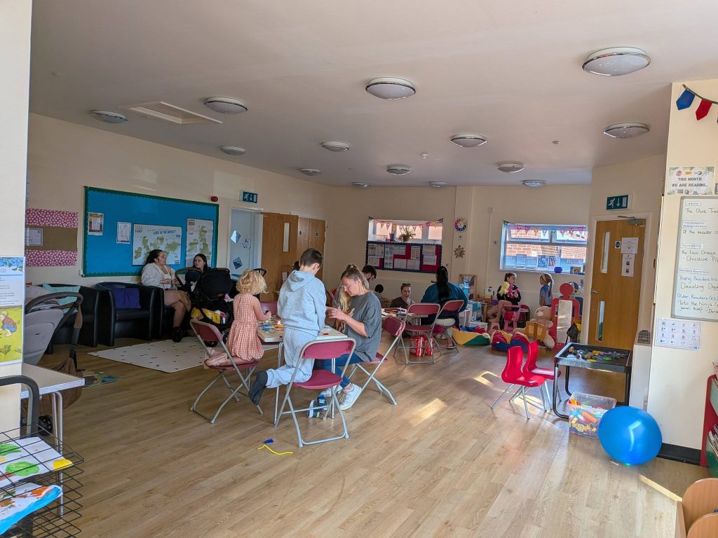 A wide view of a spacious indoor community room filled with children and adults engaged in play and craft activities.